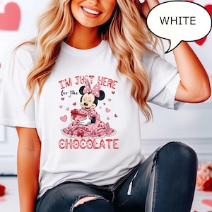 Puede incluir: Camiseta blanca con un dise&ntilde;o de Minnie Mouse. El dise&ntilde;o incluye el texto "I'M JUST HERE for the CHOCOLATE" con Minnie Mouse sosteniendo una caja de regalo en forma de coraz&oacute;n. El dise&ntilde;o es rosa y rojo.