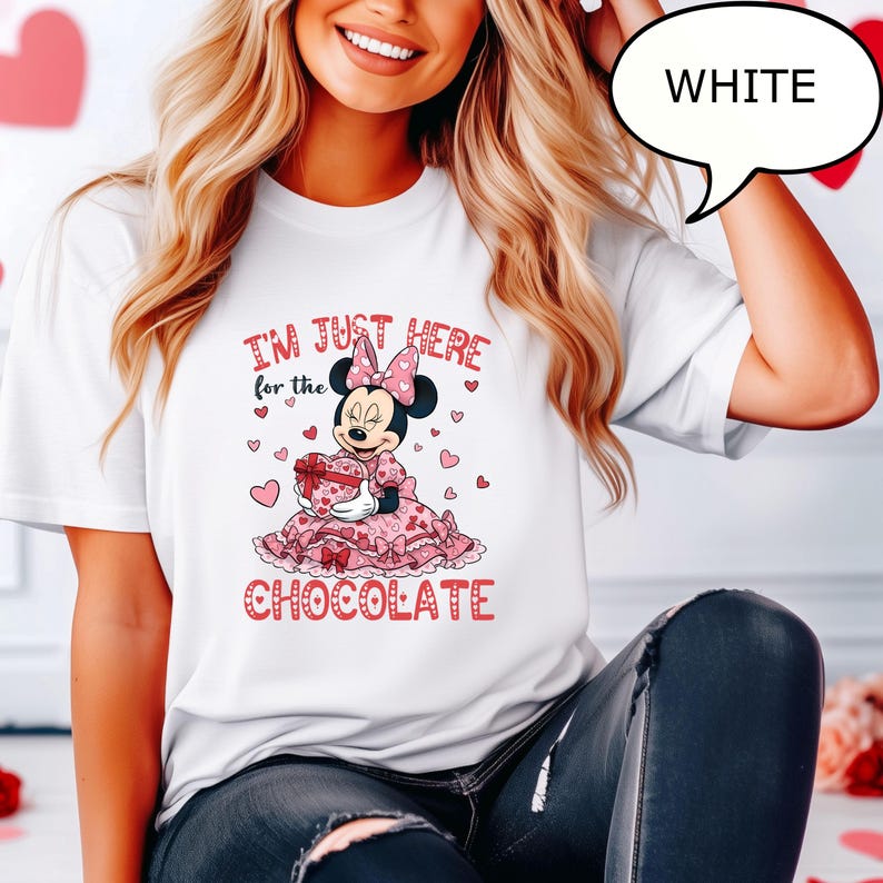 Puede incluir: Camiseta blanca con un dise&ntilde;o de Minnie Mouse. El dise&ntilde;o incluye el texto "I'M JUST HERE for the CHOCOLATE" con Minnie Mouse sosteniendo una caja de regalo en forma de coraz&oacute;n. El dise&ntilde;o es rosa y rojo.