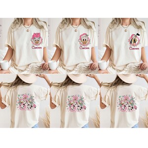 K&ouml;nnte beinhalten: Cremefarbene T-Shirts mit Disney-Figuren. Auf der Vorderseite der Shirts sind Daisy Duck, Donald Duck und Pluto abgebildet, jeweils umgeben von einem Blumenkranz und dem Wort "Custom". Auf der R&uuml;ckseite der Shirts ist eine Gruppe von Disney-Figuren zu sehen.