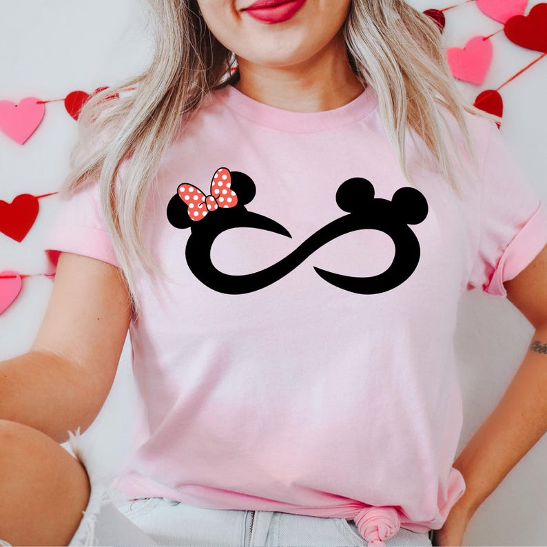 K&ouml;nnte beinhalten: Pinkes T-Shirt mit einem schwarzen Unendlichkeits-Symbol-Design mit einem Cartoon von Mickey Mouse und Minnie Mouse. Minnie Mouse tr&auml;gt eine rot-wei&szlig; gepunktete Schleife.
