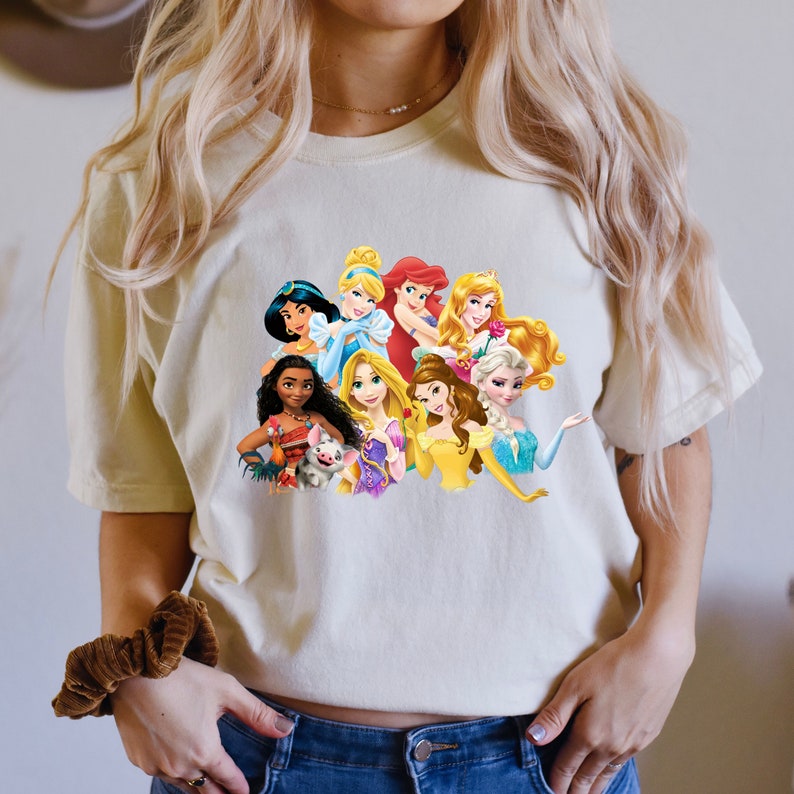 Puede incluir: Una camiseta blanca con un gr&aacute;fico colorido de princesas Disney, incluyendo Ariel, Bella, Cenicienta, Jasmine, Mulan, Pocahontas, Rapunzel, Blancanieves y Tiana.