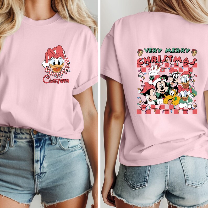 May include: A light pink t-shirt featuring a Donald Duck graphic with a Santa hat and the word "Custom" on the front. The back of the shirt has a "Very Merry Christmas" design with Mickey Mouse, Goofy, Donald Duck, and Pluto.