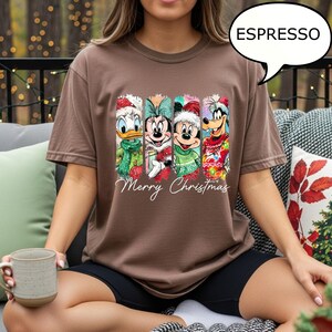 Puede incluir: Camiseta marr&oacute;n con un dise&ntilde;o navide&ntilde;o con el Pato Donald, Minnie Mouse, Mickey Mouse y Goofy. Las palabras "Merry Christmas" est&aacute;n escritas debajo de los personajes. La camiseta es de corte holgado y de color marr&oacute;n.