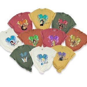 Peut inclure: Dix t-shirts diff&eacute;rents repr&eacute;sentant des princesses Disney avec leurs noms imprim&eacute;s sur chaque t-shirt. Les t-shirts sont de couleurs diff&eacute;rentes et ont un effet aquarelle avec un n&oelig;ud sur chaque t-shirt.