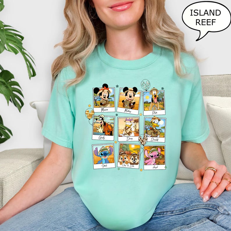 Puede incluir: Una camiseta turquesa con un gr&aacute;fico de personajes de Disney en un entorno de safari. Los personajes incluyen Mickey Mouse, Minnie Mouse, Pluto, Goofy, Donald Duck, Daisy Duck, Stitch, Chip y Dale. El texto "Island Reef" est&aacute; en un bocadillo de di&aacute;logo en la esquina superior derecha de la imagen.