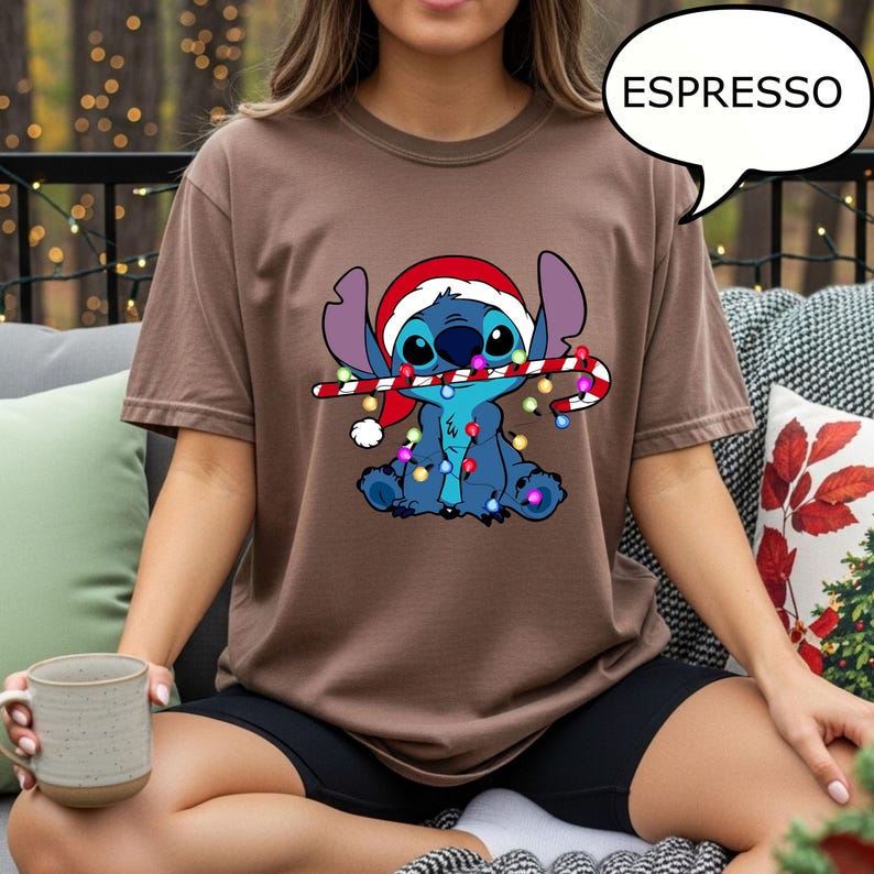 Puede incluir: Una camiseta marr&oacute;n con un personaje de dibujos animados que lleva un gorro de Pap&aacute; Noel y sostiene un bast&oacute;n de caramelo con luces navide&ntilde;as. La palabra "ESPRESSO" est&aacute; en un bocadillo. La camiseta es de color liso.