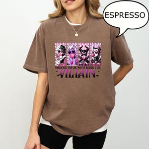 May include: Espresso-colored t-shirt featuring a graphic of four cartoon villains blowing bubblegum. The text reads "Sweetie I'm ok with being the Villain". The shirt has short sleeves and a crew neck.