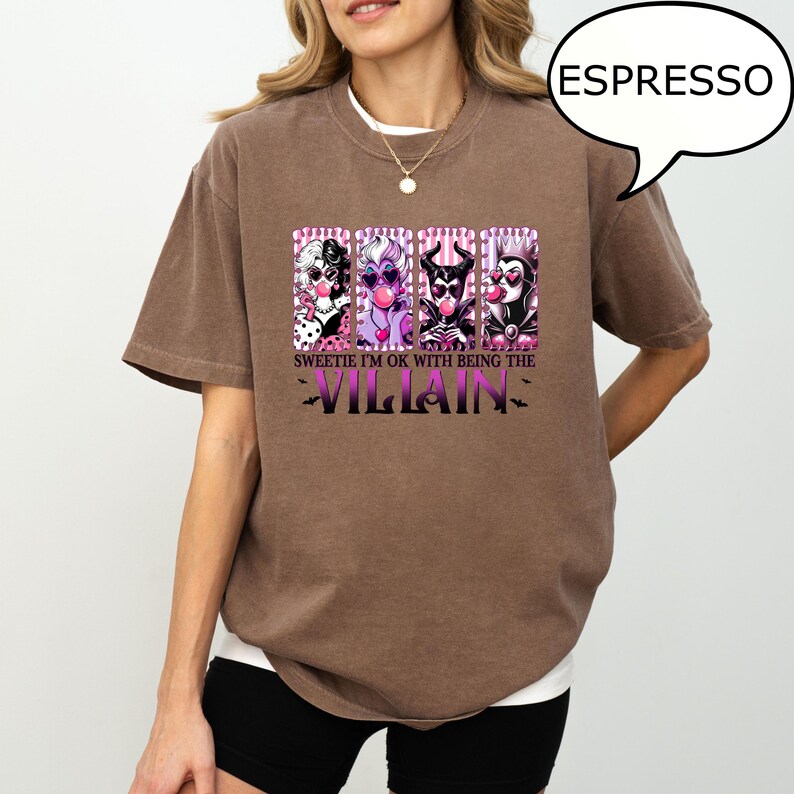 May include: Espresso-colored t-shirt featuring a graphic of four cartoon villains blowing bubblegum. The text reads "Sweetie I'm ok with being the Villain". The shirt has short sleeves and a crew neck.