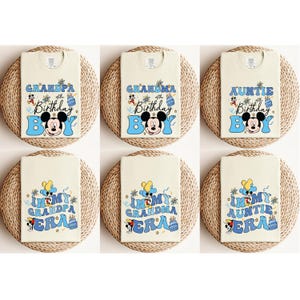 May include: Six white t-shirts with blue and yellow designs featuring Mickey Mouse. The shirts have text that reads "In My Grandpa Era", "In My Grandma Era", "In My Auntie Era", "Grandpa of the Birthday Boy", "Grandma of the Birthday Boy", and "Auntie of the Birthday Boy".