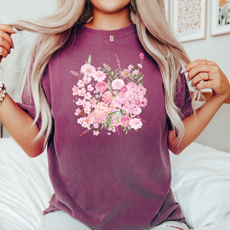 Puede incluir: Una camiseta color malva con un estampado floral de flores rosas, blancas y verdes. Las flores est&aacute;n dispuestas en forma de ramo.