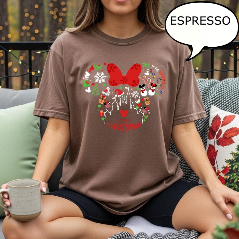 K&ouml;nnte beinhalten: Espressofarbenes T-Shirt mit festlichem Weihnachtsdesign. Das Design umfasst eine rote Schleife, Schneeflocken und die Worte "Joy to the World" und "Merry Christmas". Das Shirt hat eine bequeme Passform.