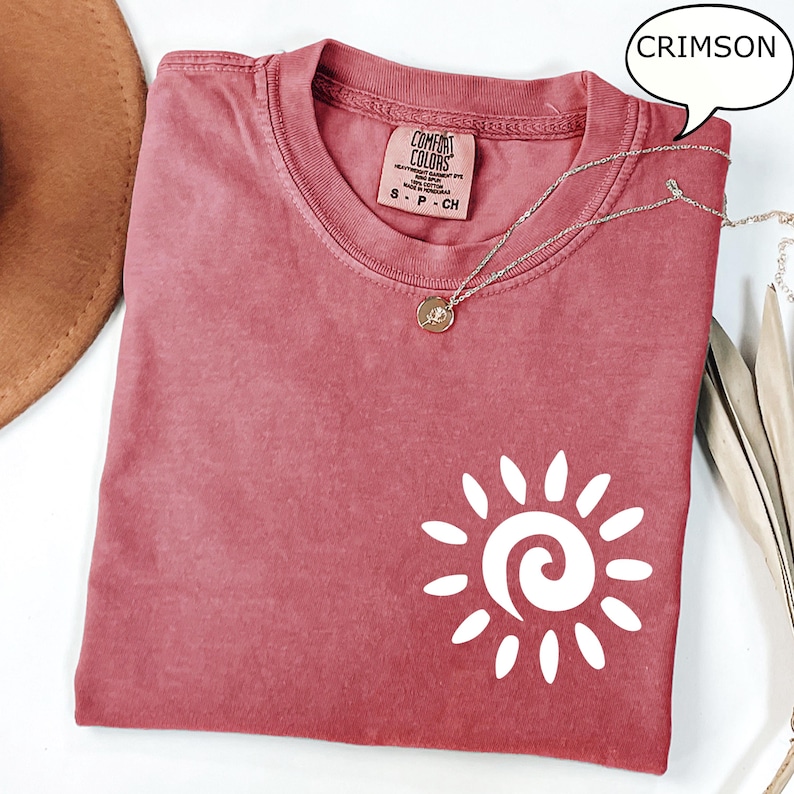 May include: A crimson colored t-shirt with a white sun graphic. The t-shirt has a distressed look and is made of a soft, comfortable fabric. The text "COMFORT COLORS" is visible on the tag.