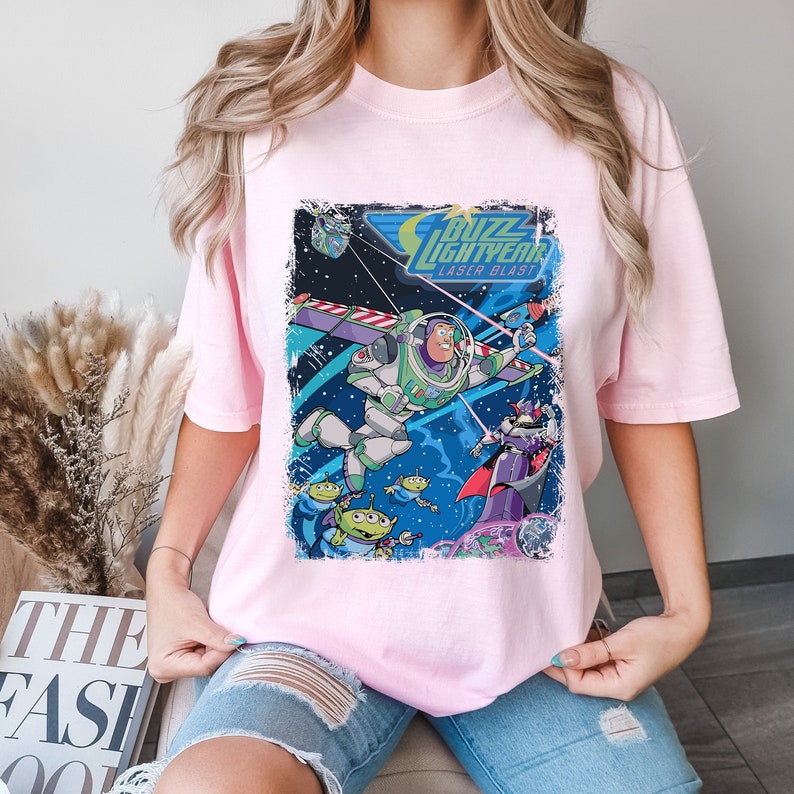 May include: Pink t-shirt with a graphic print of Buzz Lightyear from Toy Story. The graphic features Buzz Lightyear in space with the text "Buzz Lightyear Laser Blast".
