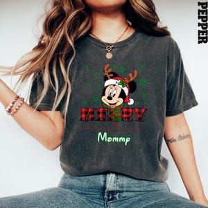 Op de afbeelding: Een donkergrijs T-shirt met een rood-zwart ruitpatroon. Het shirt heeft een cartoonafbeelding van Minnie Mouse met een kerstmanmuts en rendiergewei. De tekst "Merry Christmas Mommy" staat op het shirt gedrukt.