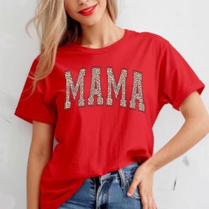 May include: Red short-sleeved t-shirt with the word "MAMA" printed in large, bold letters. The letters are outlined in black and filled with a leopard print pattern.