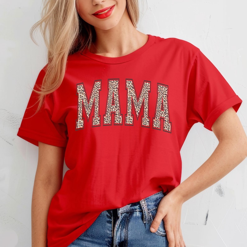 May include: Red short-sleeved t-shirt with the word "MAMA" printed in large, bold letters. The letters are outlined in black and filled with a leopard print pattern.