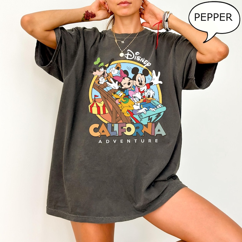 Puede incluir: Una camiseta gris oscuro con un estampado gr&aacute;fico de Mickey Mouse y sus amigos montando una monta&ntilde;a rusa. El texto "Disney California Adventure" est&aacute; impreso debajo del gr&aacute;fico.