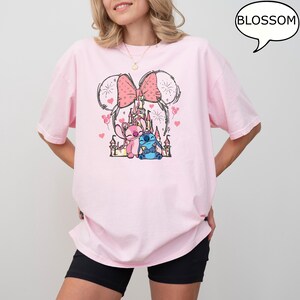 Puede incluir: Camiseta rosa claro con un gr&aacute;fico de un castillo, dos personajes de dibujos animados y un lazo con orejas de rat&oacute;n. El texto "BLOSSOM" est&aacute; en una burbuja. La camiseta est&aacute; siendo usada.