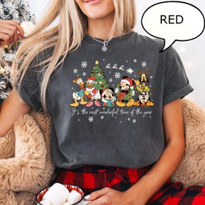 May include: Dark gray t-shirt featuring a festive graphic of Disney characters, including Mickey Mouse, Donald Duck, and Goofy, in Christmas attire. The shirt has the text "It's the most wonderful time of the year" and snowflakes.