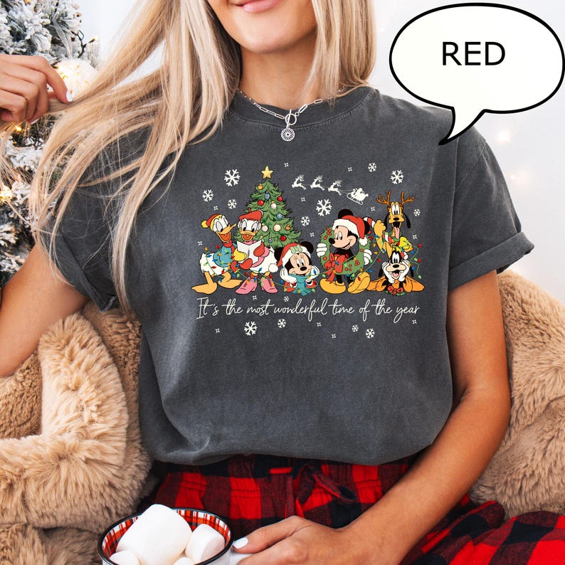 May include: Dark gray t-shirt featuring a festive graphic of Disney characters, including Mickey Mouse, Donald Duck, and Goofy, in Christmas attire. The shirt has the text "It's the most wonderful time of the year" and snowflakes.
