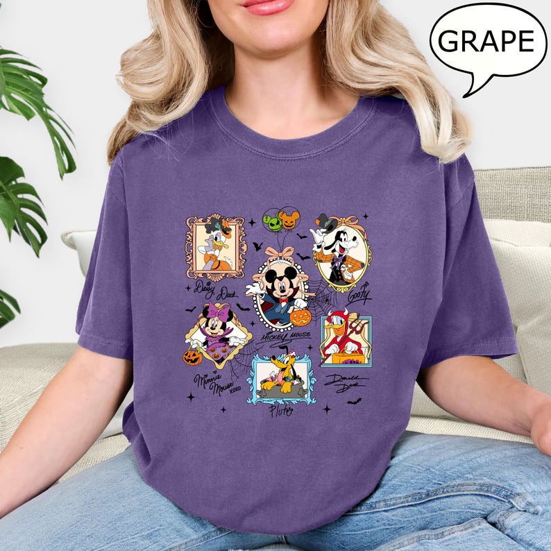 Puede incluir: Una camiseta morada con personajes de dibujos animados enmarcados, incluyendo Mickey Mouse, Donald Duck y Goofy, con acentos tem&aacute;ticos de Halloween. La camiseta tiene cuello redondo y mangas cortas. La palabra "GRAPE" est&aacute; en una burbuja.