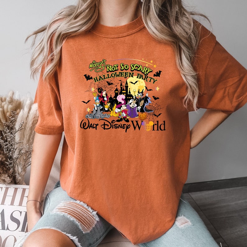 May include: Orange t-shirt with a graphic of Mickey Mouse and friends in a Halloween scene. The text reads "Mickey's Not So Scary Halloween Party Walt Disney World".