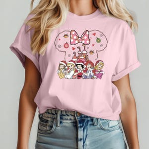 Puede incluir: Camiseta rosa con un dise&ntilde;o navide&ntilde;o con un castillo, un lazo y seis princesas Disney con gorros de Pap&aacute; Noel. Las princesas son Blancanieves, Cenicienta, Ariel, Bella, Aurora y Rapunzel.