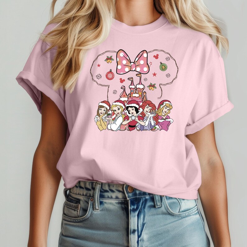 Puede incluir: Camiseta rosa con un dise&ntilde;o navide&ntilde;o con un castillo, un lazo y seis princesas Disney con gorros de Pap&aacute; Noel. Las princesas son Blancanieves, Cenicienta, Ariel, Bella, Aurora y Rapunzel.