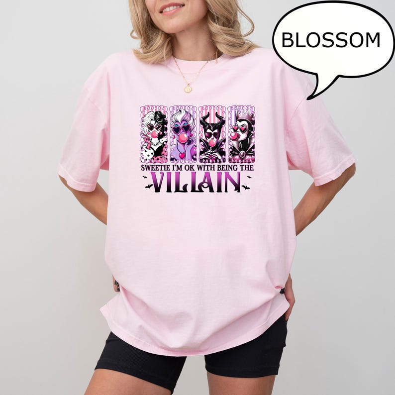 May include: A light pink t-shirt featuring a graphic of four cartoon villains with bubblegum. The text "Sweetie I'm OK with being the Villain" is printed below the characters in purple. A speech bubble says "BLOSSOM".