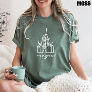 May include: A green t-shirt with a white outline of Cinderella's castle and the word "magic" underneath.