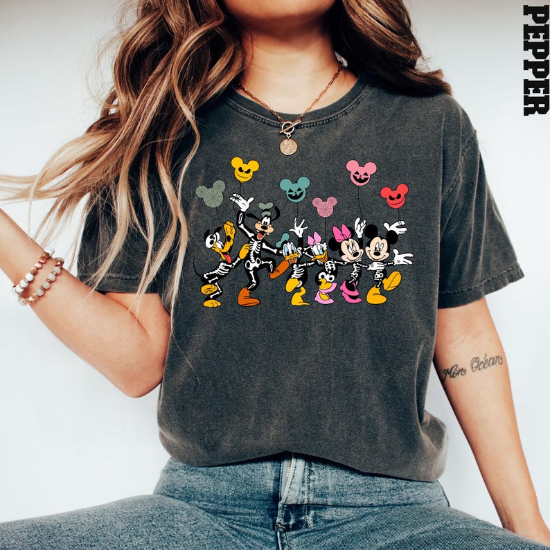 May include: A dark gray t-shirt with a graphic print of Mickey Mouse, Minnie Mouse, Donald Duck, and Goofy dressed as skeletons holding colorful balloons. The text "Pepper" is visible in the upper right corner of the image.