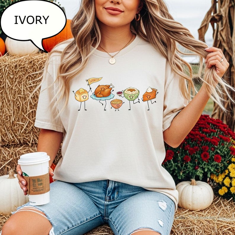 Pu&ograve; includere: Una t-shirt color avorio con una stampa grafica di cibi del Ringraziamento antropomorfi, tra cui un tacchino arrosto che tiene una bandierina gialla con la scritta THANKFUL, un panino, una ciotola di pur&egrave; di patate, ripieno e una fetta di torta di zucca.