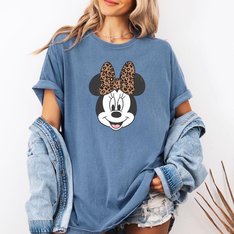 May include: A blue t-shirt with a cartoon image of Minnie Mouse. Minnie Mouse is wearing a leopard print bow.