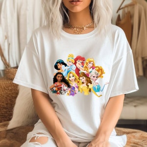 Puede incluir: Camiseta blanca con un estampado gr&aacute;fico colorido de princesas Disney, incluyendo Cenicienta, Ariel, Bella y Jasmine.