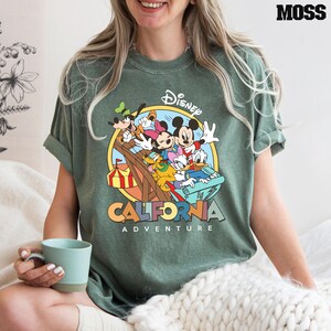 Puede incluir: Camiseta verde con un gr&aacute;fico de estilo vintage de Mickey Mouse y sus amigos montando una monta&ntilde;a rusa. El texto "Disney California Adventure" est&aacute; impreso debajo de la imagen.