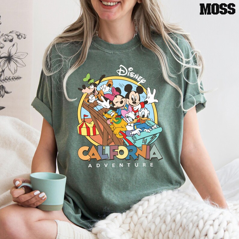 Puede incluir: Camiseta verde con un gr&aacute;fico de estilo vintage de Mickey Mouse y sus amigos montando una monta&ntilde;a rusa. El texto "Disney California Adventure" est&aacute; impreso debajo de la imagen.
