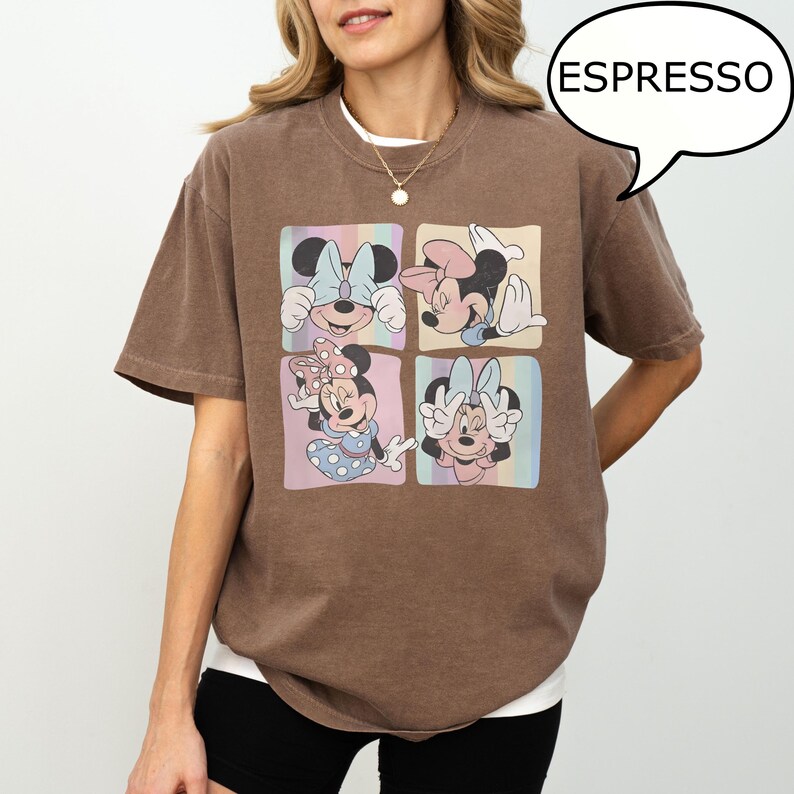 Puede incluir: Camiseta color espresso con un gr&aacute;fico de cuatro paneles de Minnie Mouse en varias poses. Cada panel tiene un fondo de arco&iacute;ris pastel. La camiseta tiene un corte holgado y se ve una camiseta interior blanca.