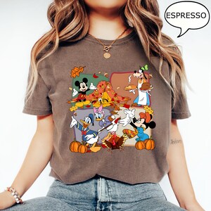 May include: Espresso-colored t-shirt featuring a colorful graphic of Disney characters celebrating autumn. Mickey Mouse, Donald Duck, and Goofy are depicted with pumpkins and fall leaves. The word "ESPRESSO" is in a speech bubble.