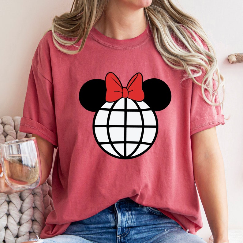K&ouml;nnte beinhalten: Ein rotes T-Shirt mit einer schwarzen und wei&szlig;en Globusgrafik mit einer roten Schleife oben, die an Mickey-Maus-Ohren erinnert.