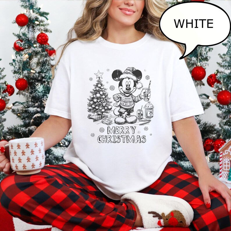Puede incluir: Camiseta blanca con un gr&aacute;fico navide&ntilde;o de Mickey Mouse en blanco y negro, sosteniendo una bebida y un &aacute;rbol de Navidad. El texto "MERRY CHRISTMAS" est&aacute; debajo. Un bocadillo dice "WHITE".