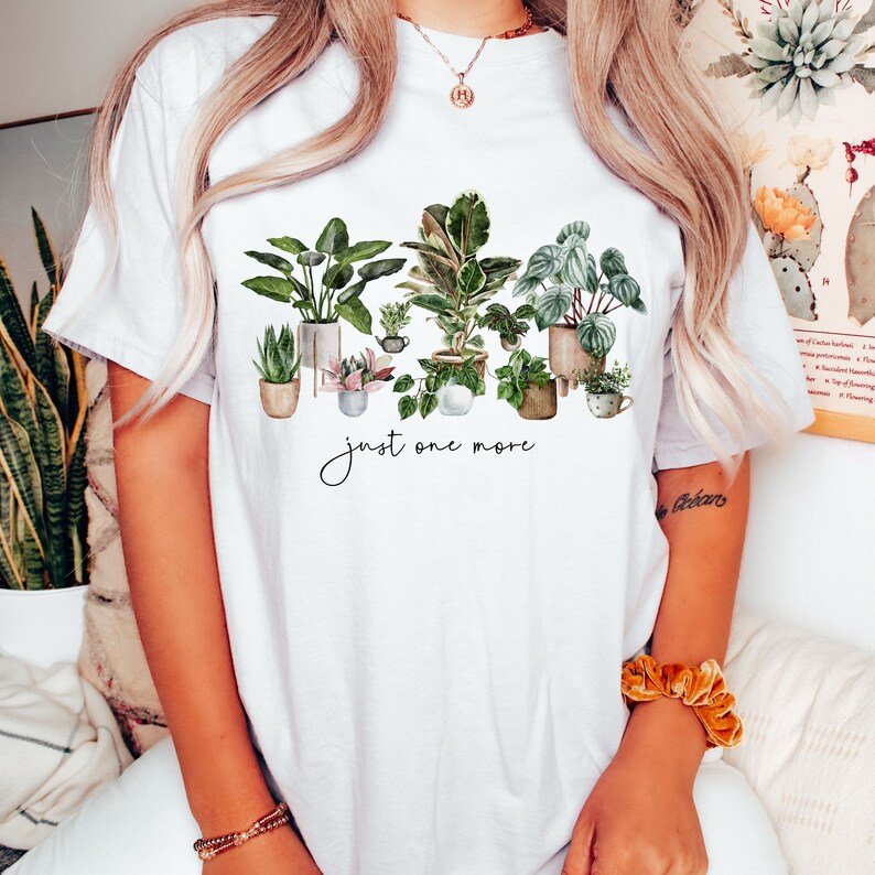 May include: White t-shirt with a watercolor illustration of potted plants and the text "just one more".