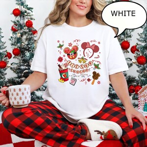 May include: White t-shirt with a festive graphic featuring a gingerbread Mickey Mouse, Minnie Mouse ears, and the text "'Tis the Season". The shirt also includes a coffee cup, a calendar, and a popsicle.
