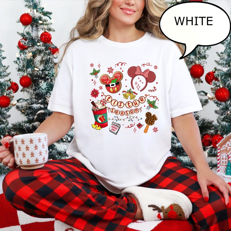 May include: White t-shirt with a festive graphic featuring a gingerbread Mickey Mouse, Minnie Mouse ears, and the text "'Tis the Season". The shirt also includes a coffee cup, a calendar, and a popsicle.