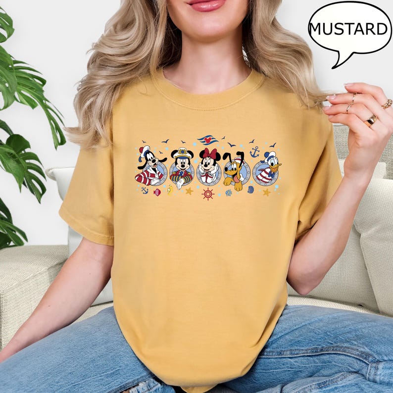 May include: Mustard-colored t-shirt featuring a nautical-themed graphic with cartoon characters in circular frames. The graphic includes characters like Mickey Mouse, Minnie Mouse, and Donald Duck, along with anchors and seagulls. The word "MUSTARD" is in a speech bubble.