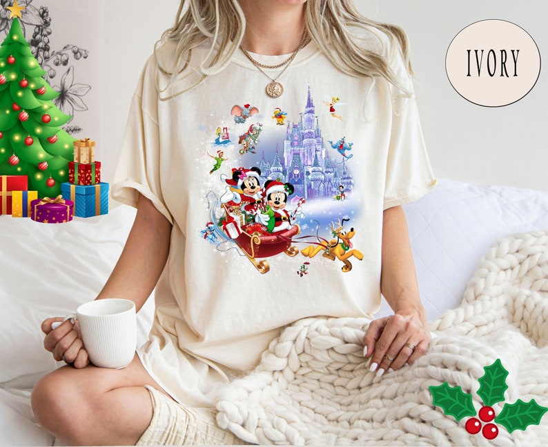 Puede incluir: Una camiseta blanca con un dise&ntilde;o navide&ntilde;o que presenta a Mickey Mouse y Minnie Mouse en un trineo, rodeados de otros personajes de Disney, incluidos Pluto, Donald Duck y Goofy. El dise&ntilde;o tambi&eacute;n incluye un castillo nevado y el texto "IVORY".