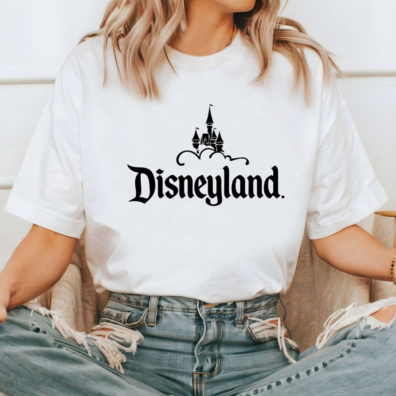 Puede incluir: Camiseta blanca con un dise&ntilde;o negro del castillo de Disneyland y la palabra "Disneyland". La camiseta est&aacute; hecha de un material suave, adecuada para ropa casual. El dise&ntilde;o es un logotipo cl&aacute;sico de parque tem&aacute;tico.