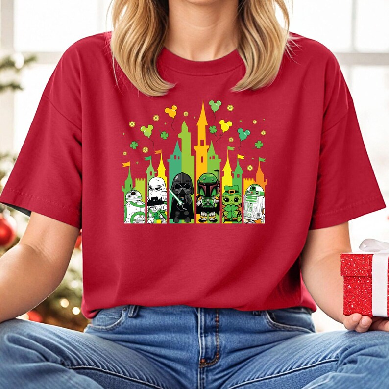 Puede incluir: Camiseta roja con un gr&aacute;fico colorido de personajes de Star Wars frente a un castillo. El dise&ntilde;o incluye a Darth Vader, Boba Fett y R2-D2. Hay detalles en verde, amarillo y naranja.