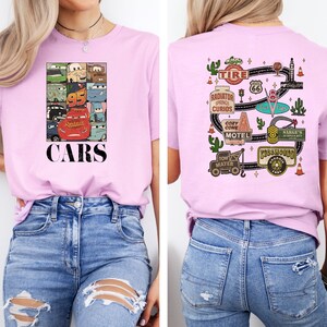 Puede incluir: Camiseta rosa con un estampado de Cars en la parte delantera y un dise&ntilde;o inspirado en la Ruta 66 en la parte trasera. La parte delantera presenta un collage de personajes de Cars, incluyendo Rayo McQueen, Mate y Doc Hudson. La parte trasera presenta una carretera con varios puntos de referencia de la pel&iacute;cula, incluyendo Radiador Springs, el Motel Cozy Cone y la tienda de excedentes de Sarge.