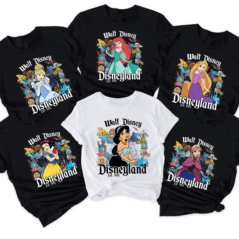 May include: Several black and white t-shirts showcasing Disney princesses. Each shirt has a princess graphic and the text "Walt Disney Disneyland Est. 1955". The princesses featured are Ariel, Cinderella, Rapunzel, Snow White, Jasmine, and Anna.