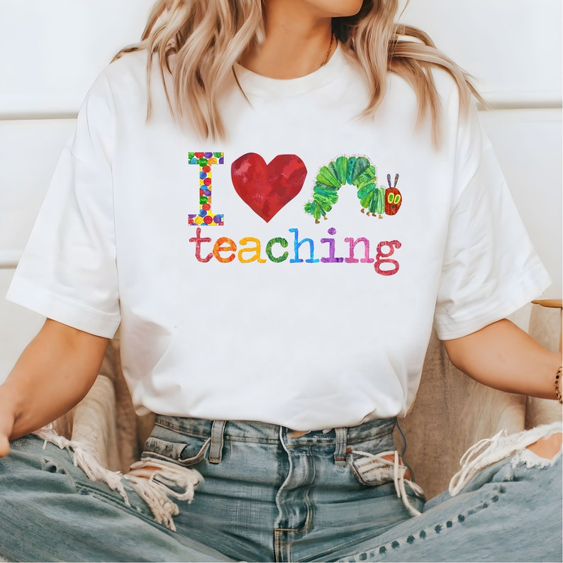 Op de afbeelding: Wit T-shirt met een kleurrijke afbeelding met de tekst "Ik hou van lesgeven" met een rood hart en een groene rups.